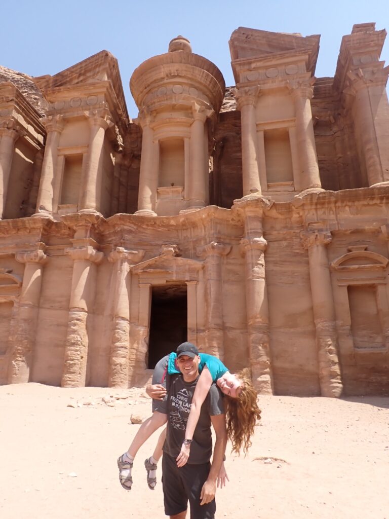 Two tourists doing a fireman's carry technique in front of the Monastery (Deir) in Petra