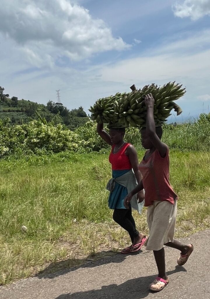 Two women carrying items on their heads on the road in Uganda in 2025